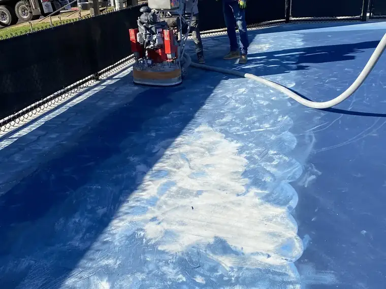 Crew grinding the blue surface off a pickleball court in bright sun