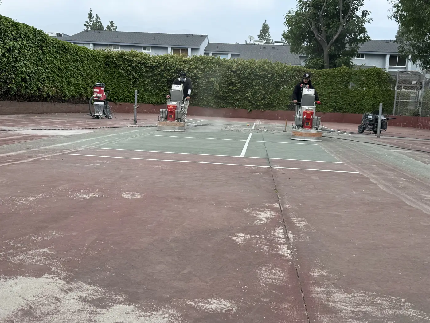 Green painted tennis court with white lines and grinding machines set up along the baseline