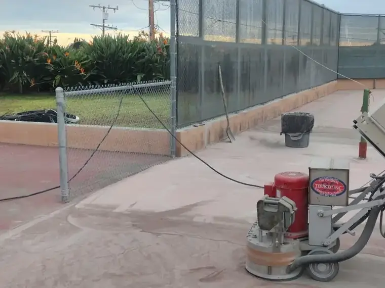 Grinding equipment on a court beside a chain link fence and lawn