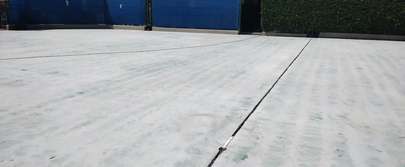 Court surface ground back to clean gray concrete against a blue wall