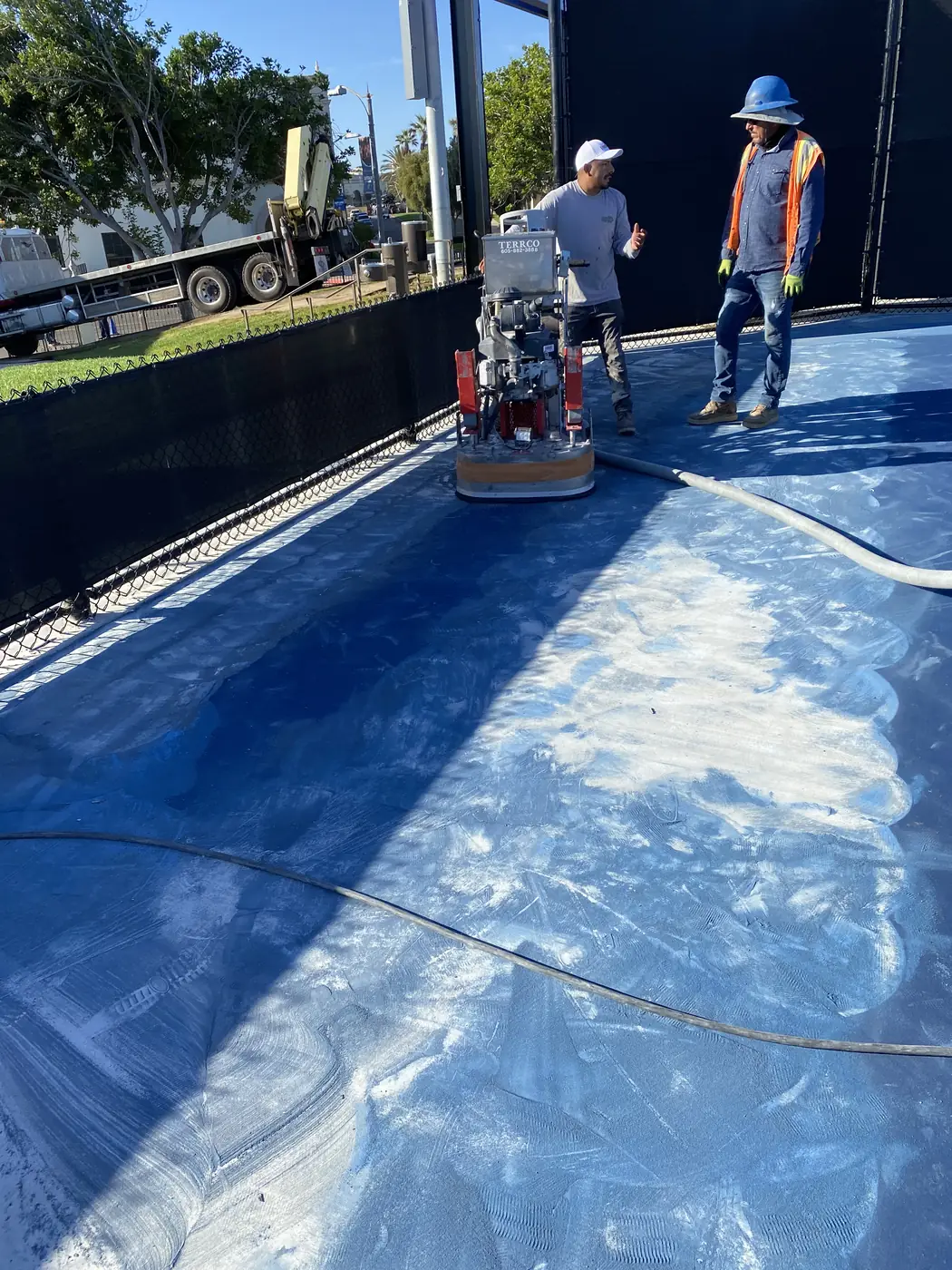 Grinder cutting a pale stripe through the blue coating on a sports court