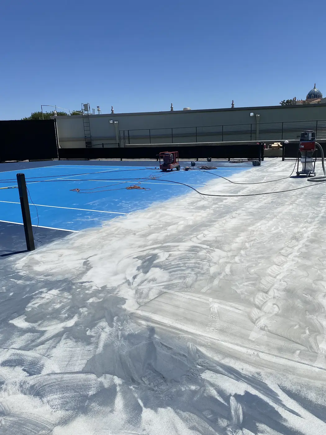 Blue sports court with a wide band of coating already ground away