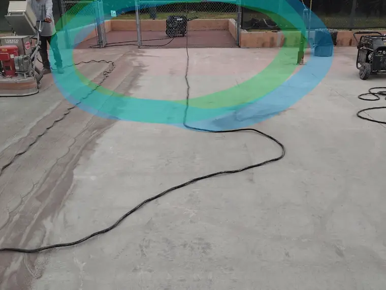 Crew grinding a pool deck with the old teal and green coating still visible