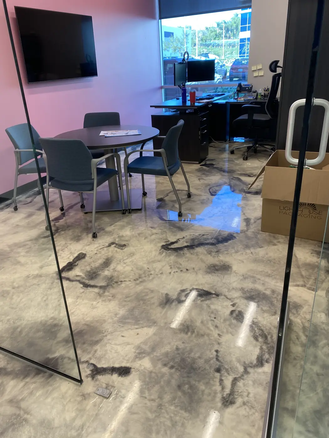 Metallic epoxy floor reflecting the ceiling lights beside a glass meeting room