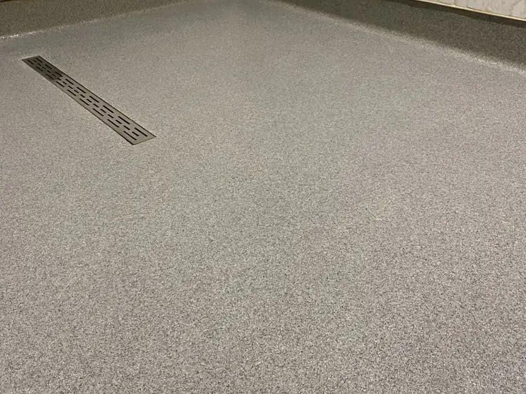 Gray flake epoxy floor with a stainless trench drain and coved wall base