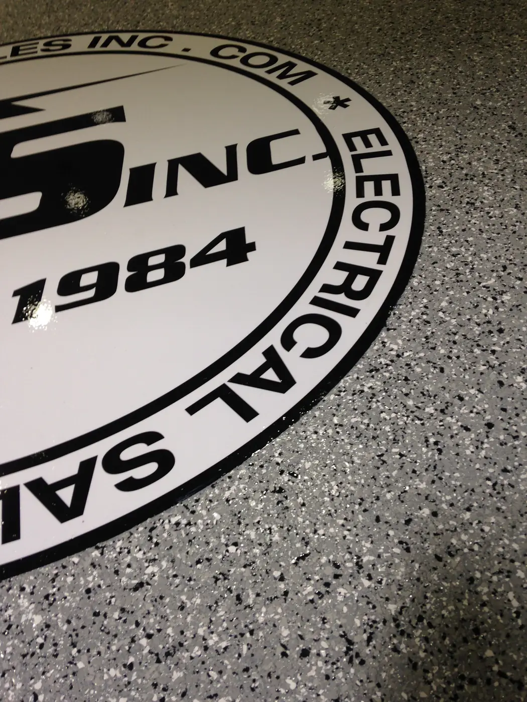 Close view of an electrical company logo inlaid into a gray flake epoxy floor
