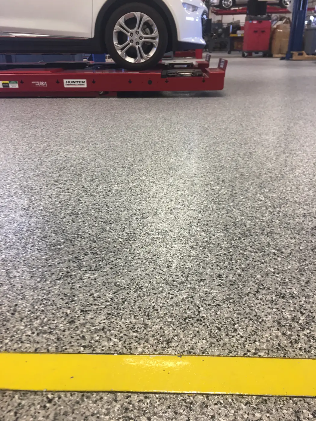 Gray flake epoxy floor beneath a wheel alignment rack in a service shop