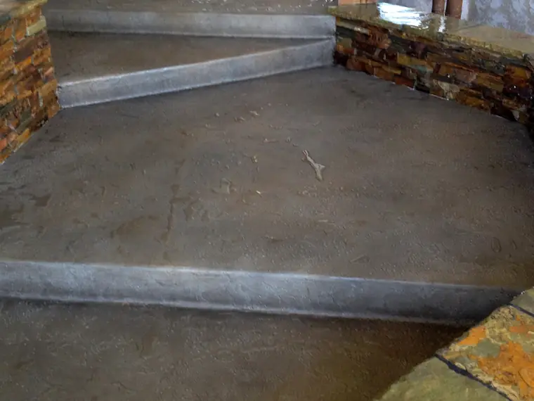 Gray and brown stained entry steps beside a stone-faced planter