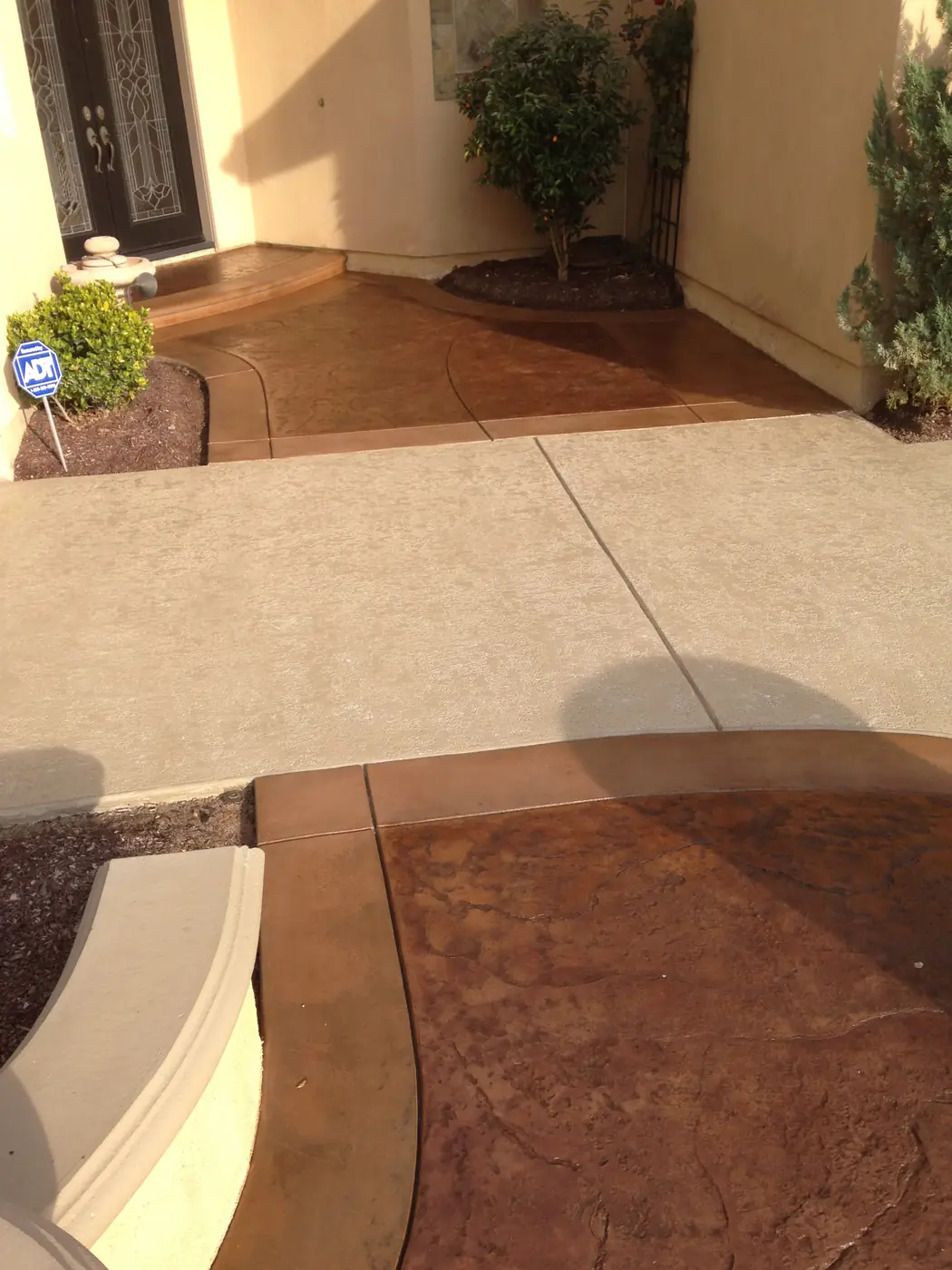Stained front entry walkway in warm brown meeting a cream patio