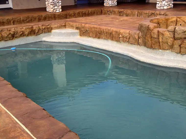 Stained pool deck under a covered patio with stone-faced columns