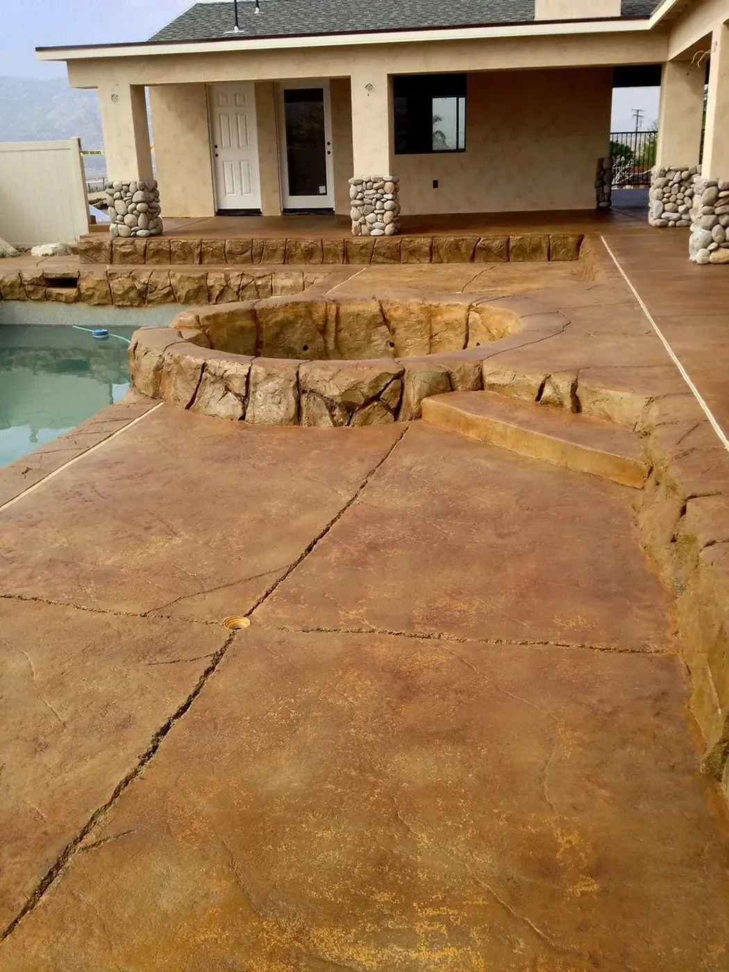 Brown stained and scored patio beside a pool with rock coping