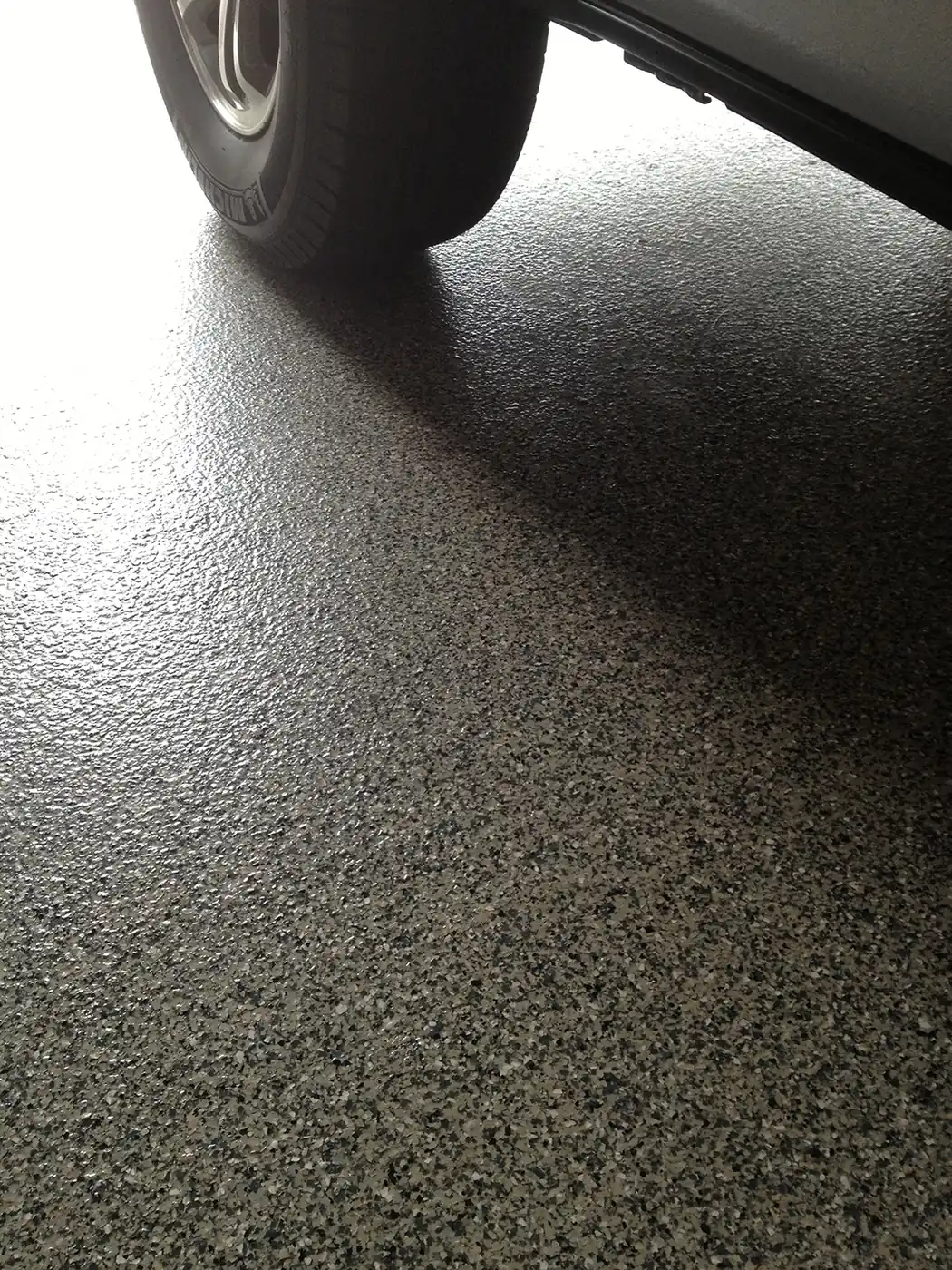 Car tire resting on a gray flake epoxy garage floor
