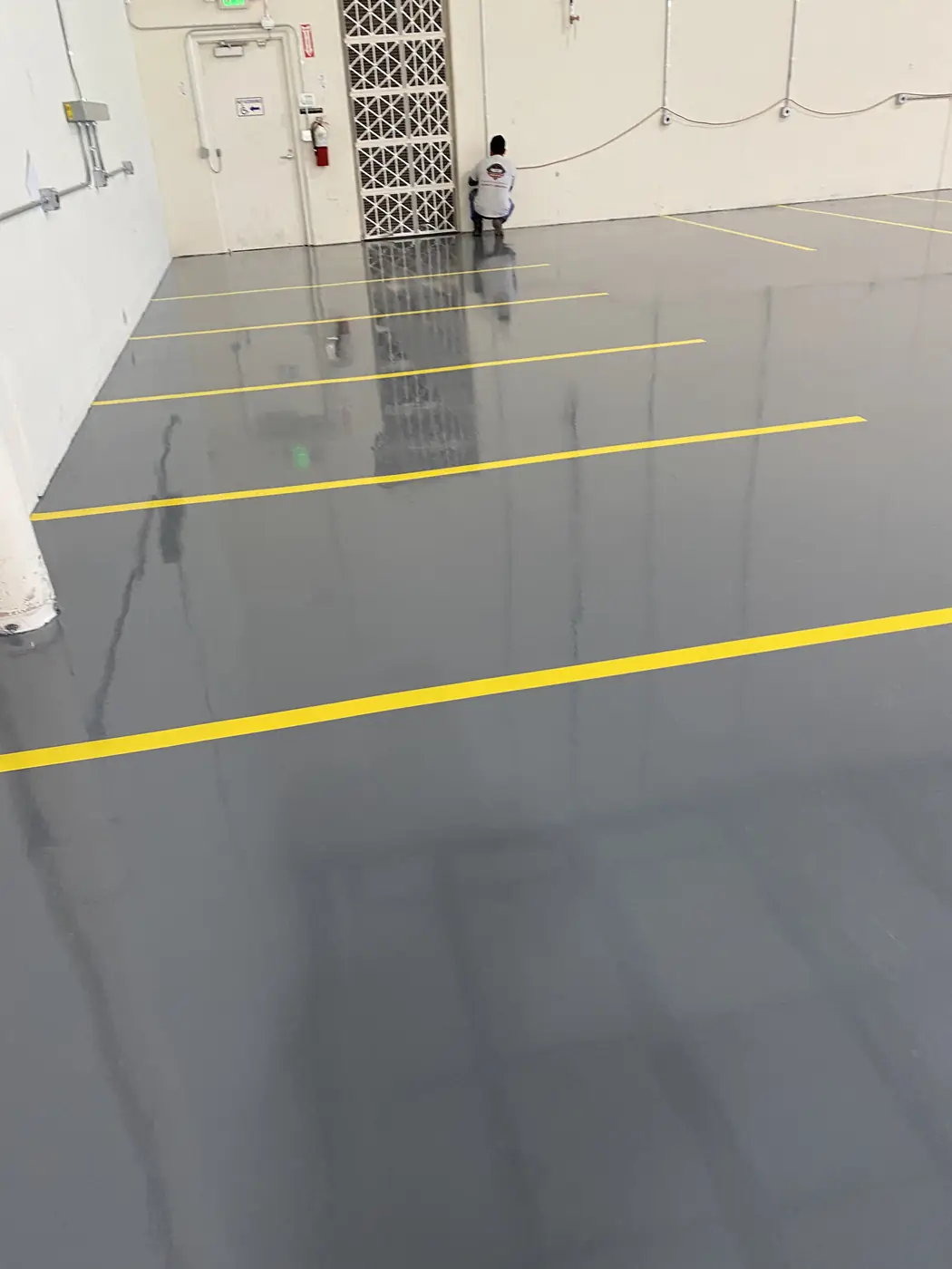 Gray epoxy warehouse floor with yellow striping and a worker in the distance
