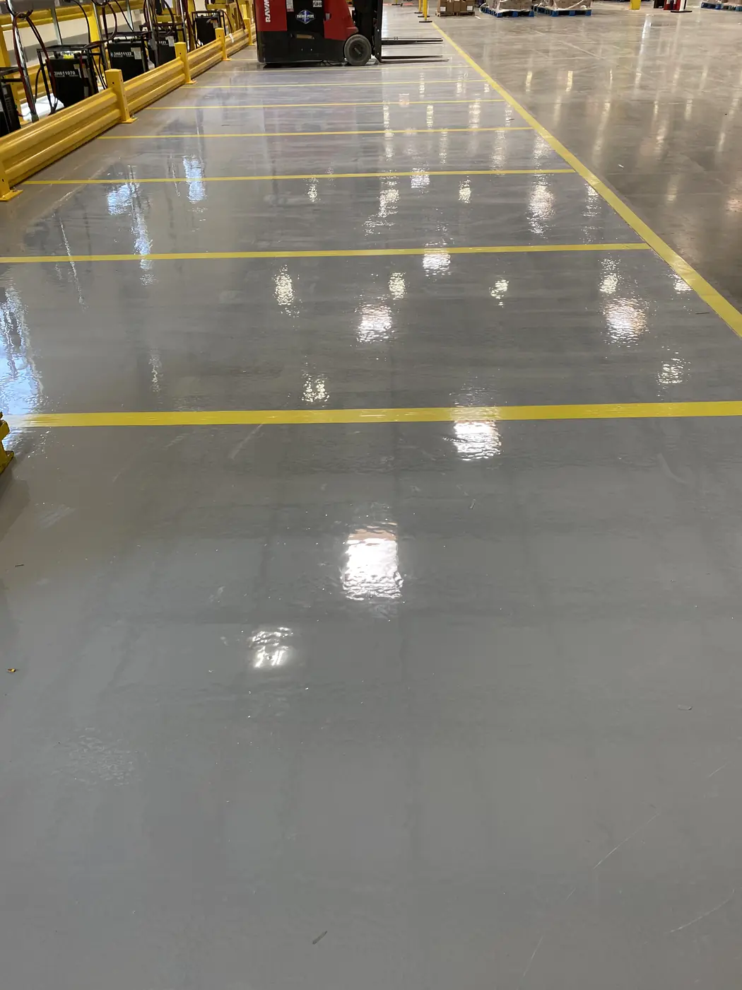High-gloss gray epoxy warehouse floor reflecting the overhead lights between yellow lines