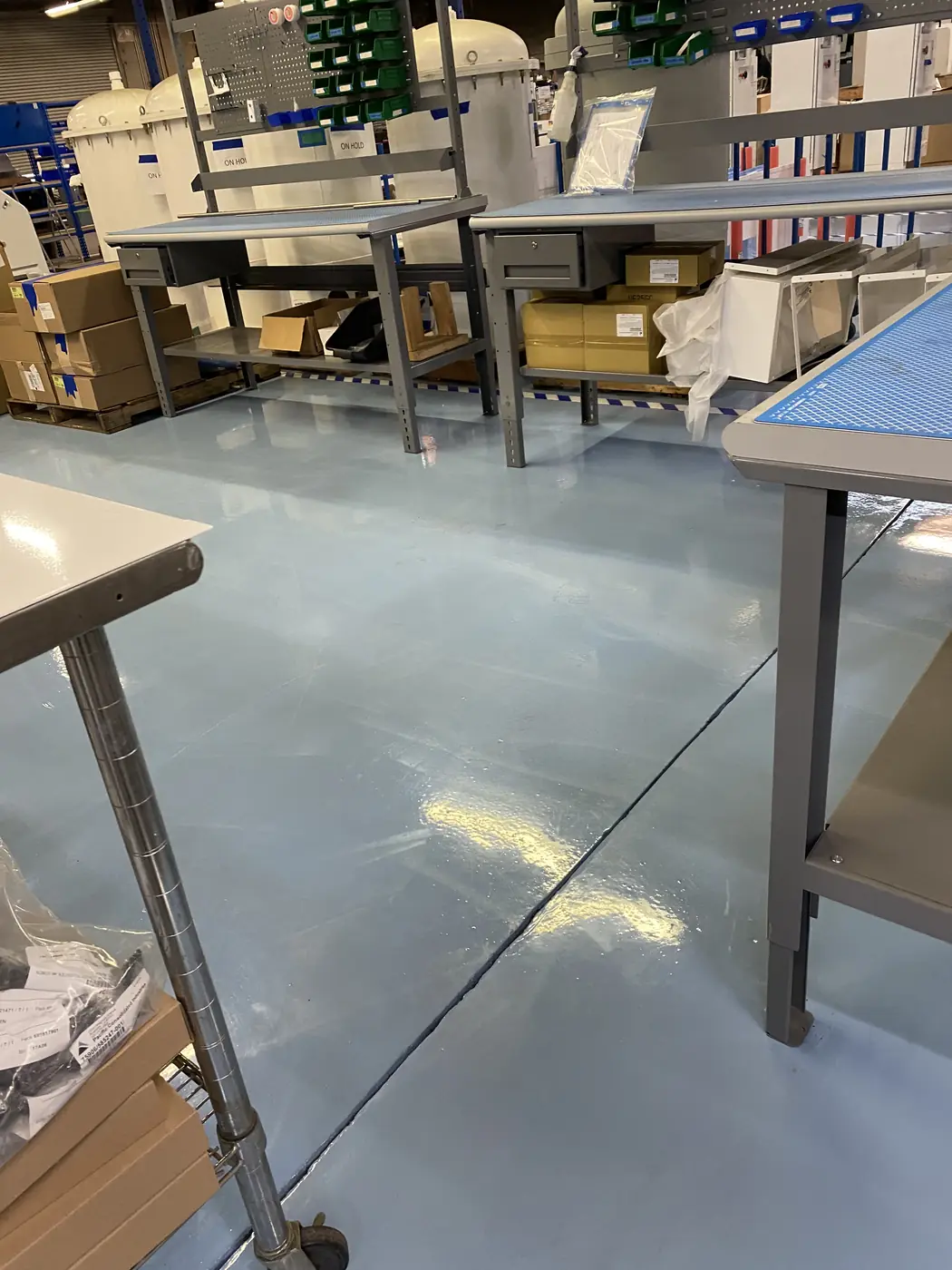 Pale blue epoxy floor beneath stainless workbenches in a production area