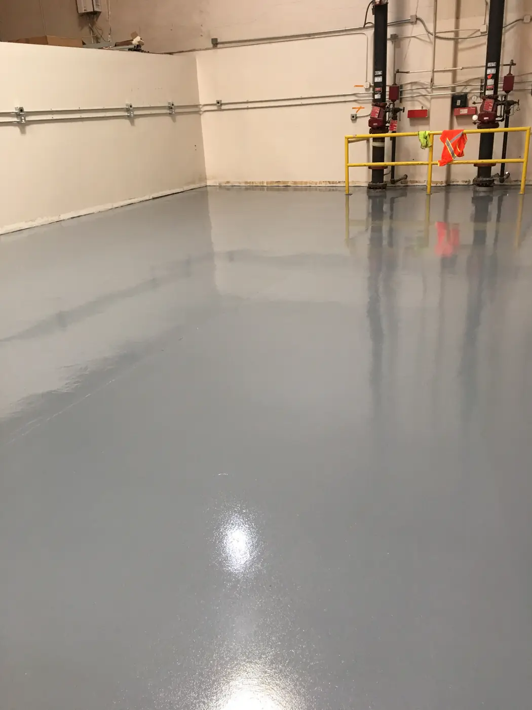Gray epoxy floor in a warehouse bay with yellow guard rails at the far wall