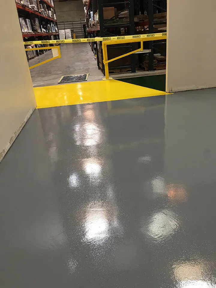Gray warehouse epoxy floor with a single yellow line marking the walkway