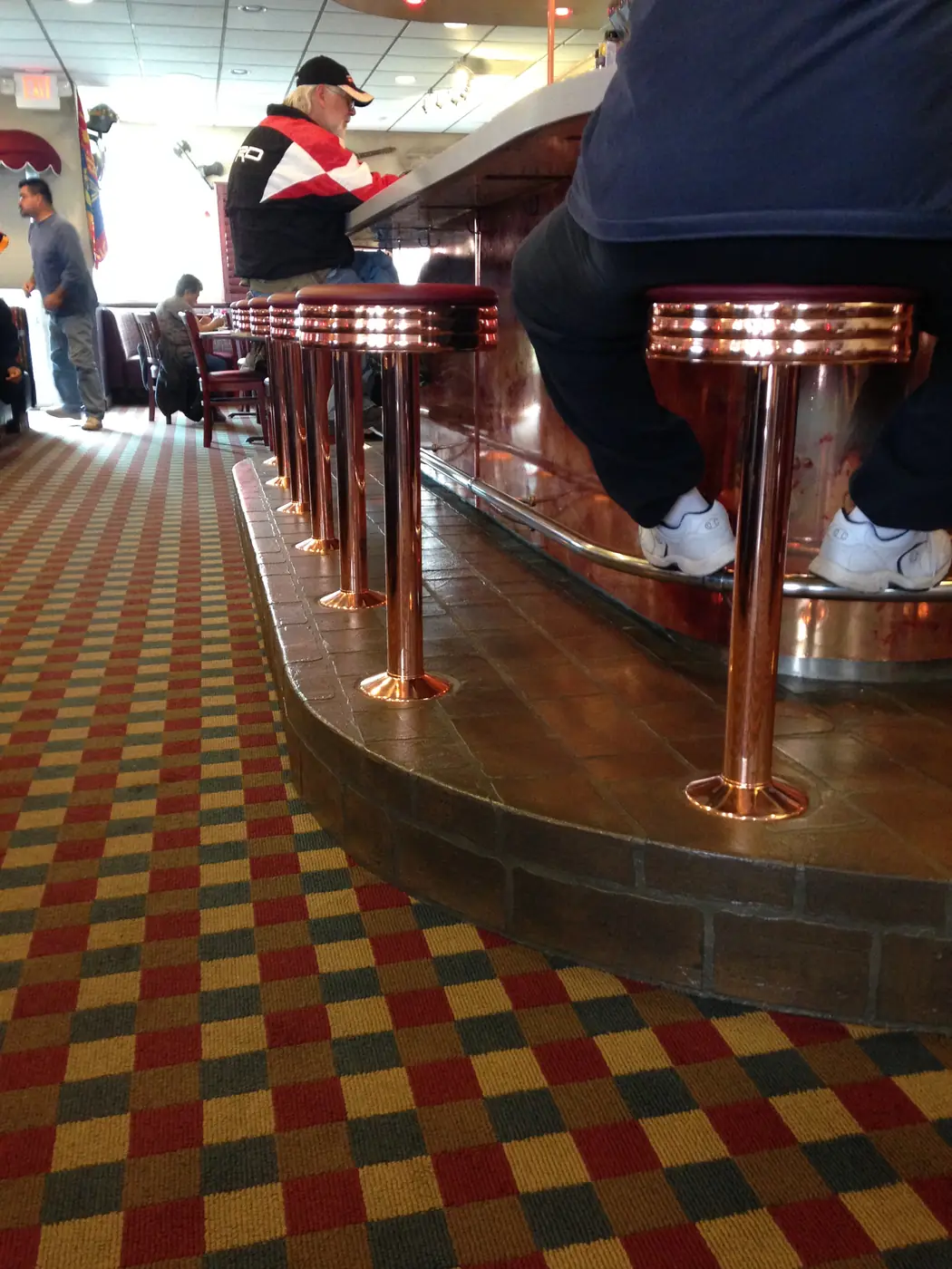 Diner counter with copper stools standing on a red and gold checcurboard floor overlay