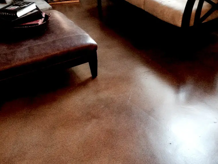 Brown stained concrete living room floor with a leather ottoman