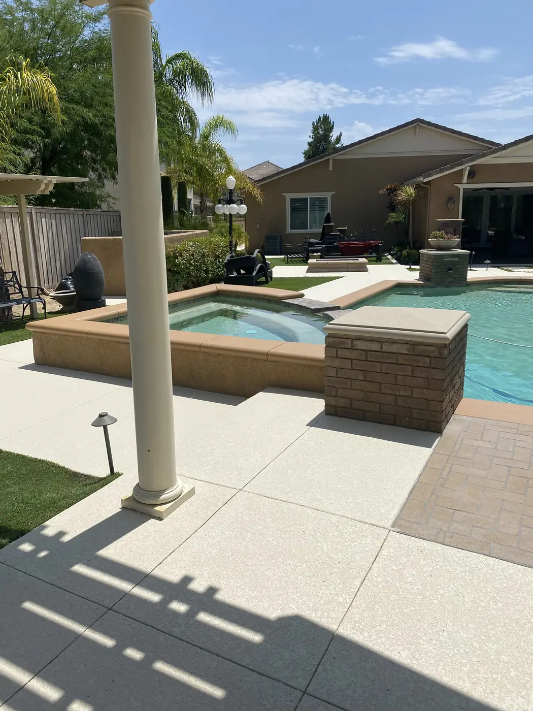 Pool and spa seen from a covered patio with a cream textured deck