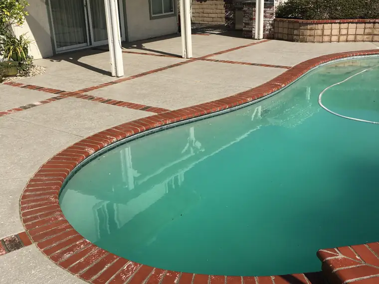 Kidney-shaped pool with red brick coping and a light gray textured deck