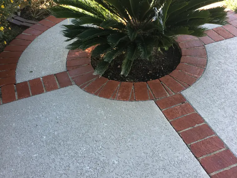 Gray textured deck with red brick banding around a palm planter