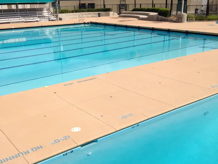 Commercial lap pool with a wide tan textured deck and stainless handrails