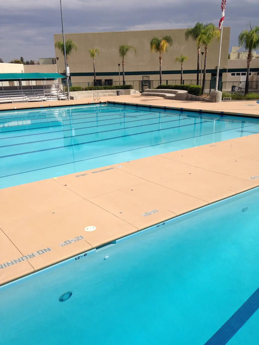 Commercial lap pool with a wide tan textured deck and stainless handrails