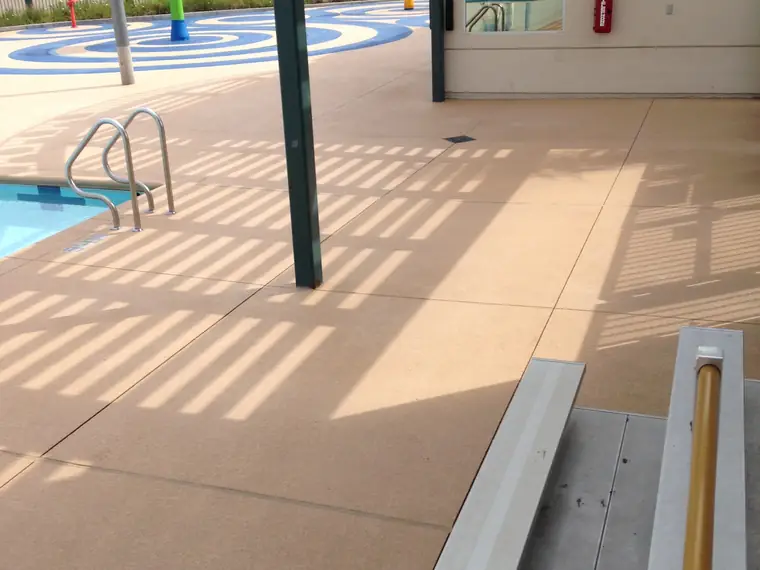 Splash pad and diving board area on a tan textured commercial pool deck