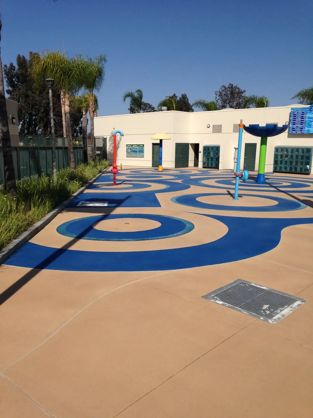 Blue swirl splash pad set into a tan deck outside a community building