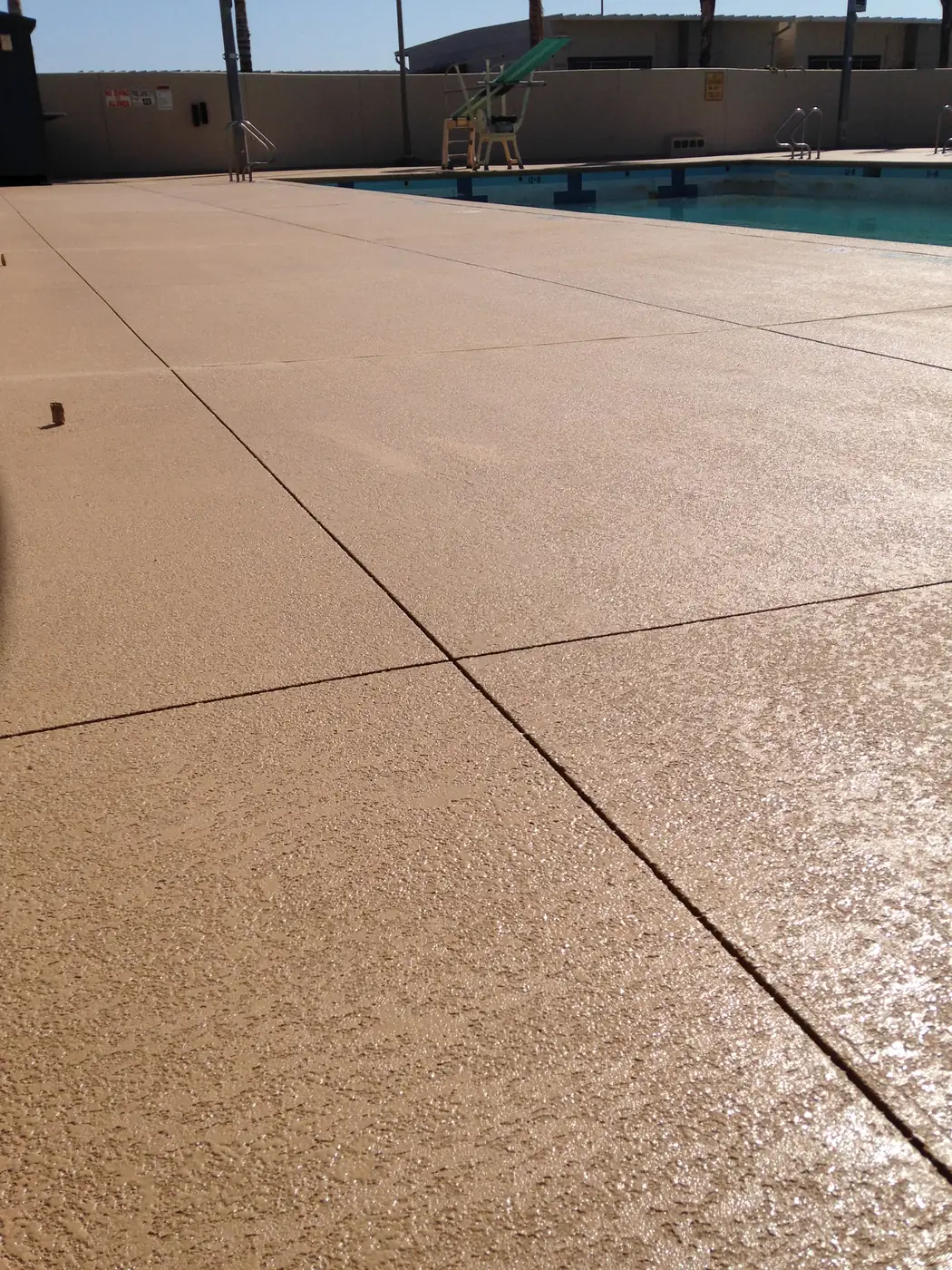 Wide tan textured pool deck running to the water's edge