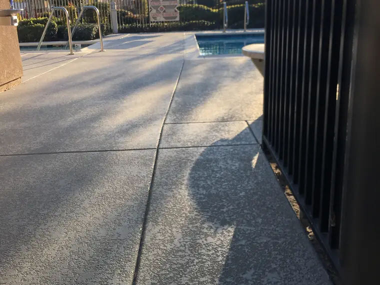 Gray speckled pool deck seen past a black metal fence