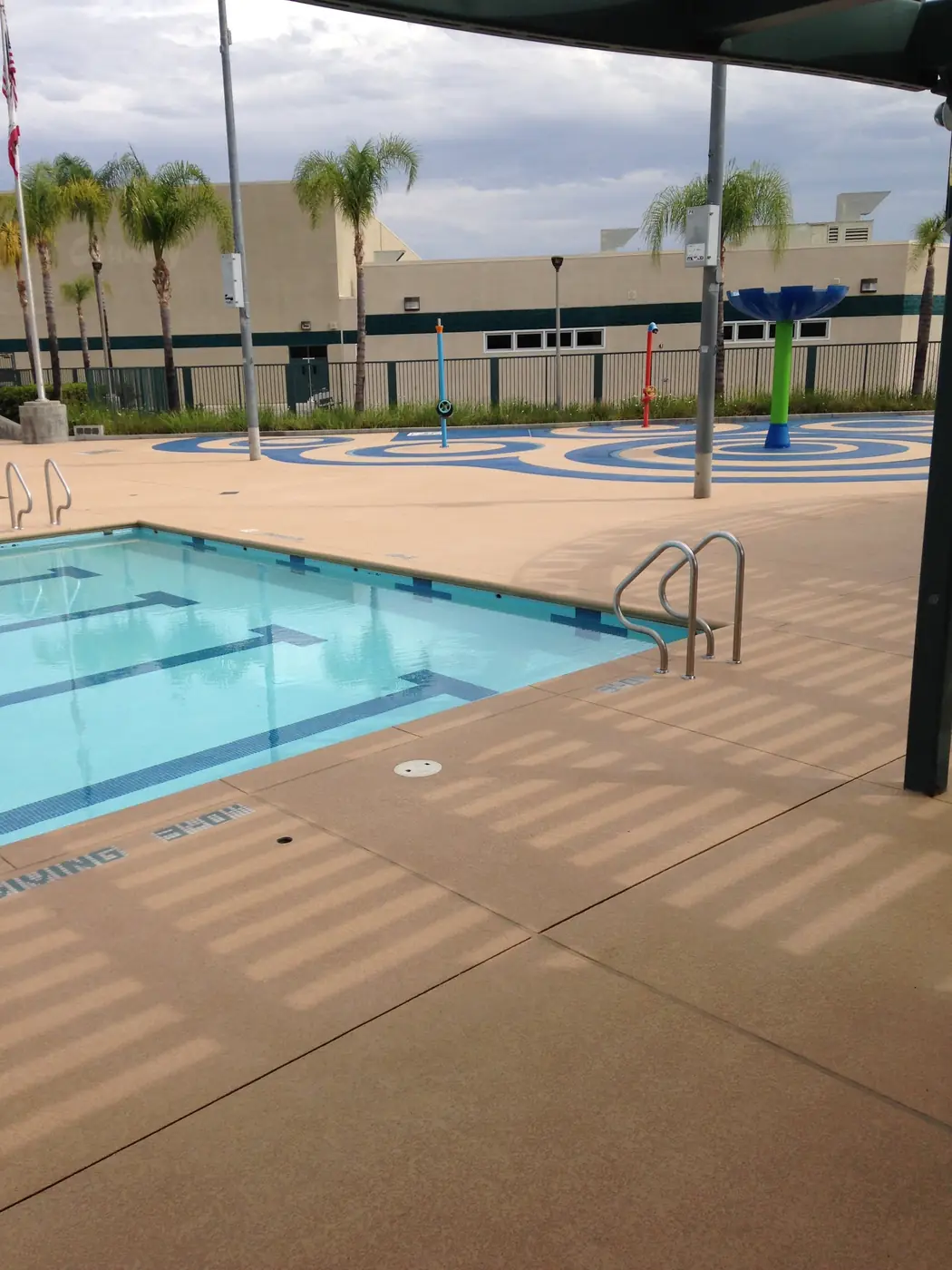 Wide view of a community pool and splash pad with a tan coated deck