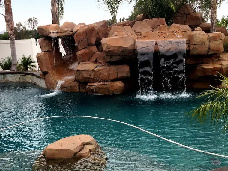 Rock waterfall with twin falls running into a pool framed by palms