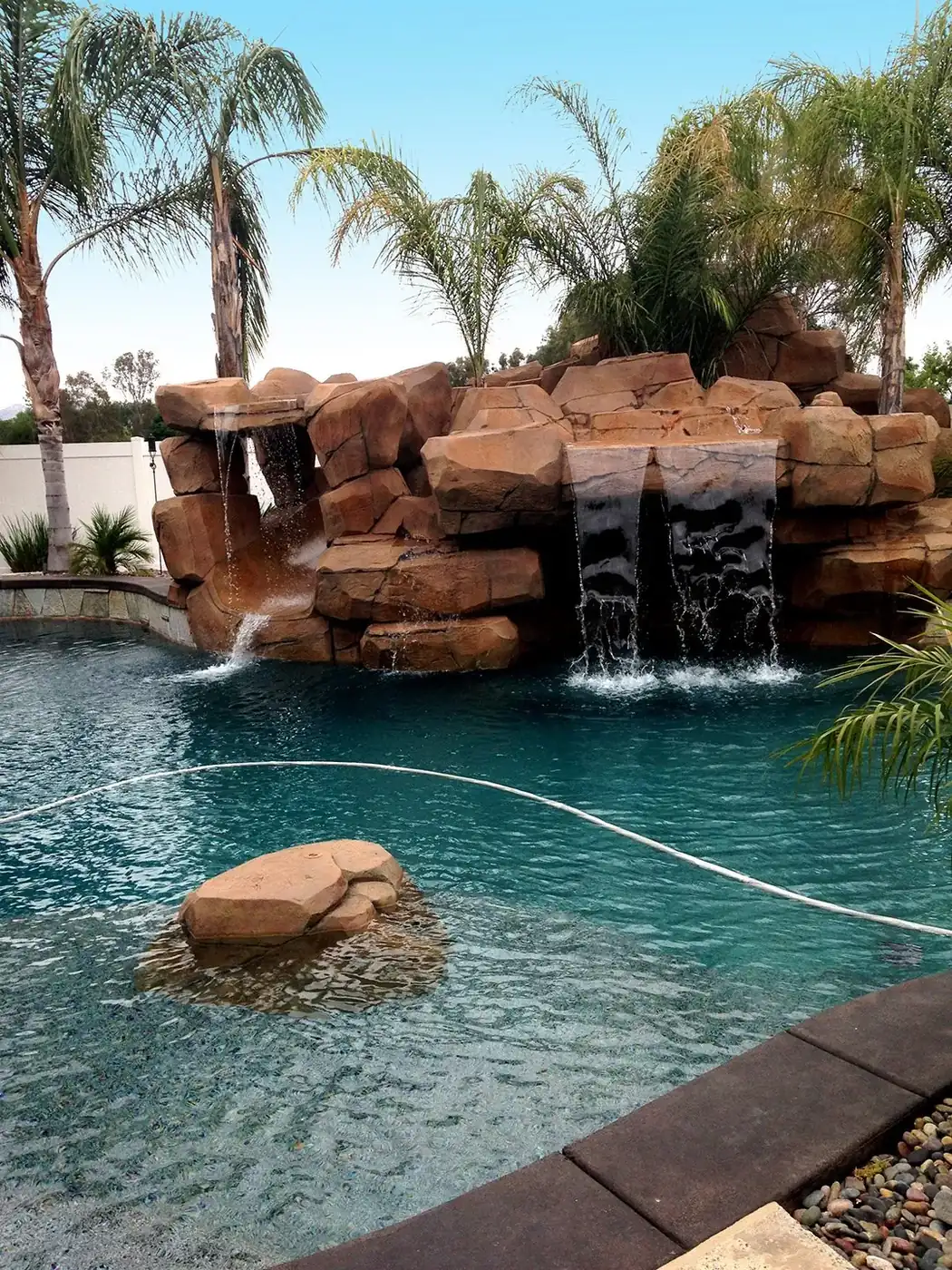 Rock waterfall with twin falls running into a pool framed by palms