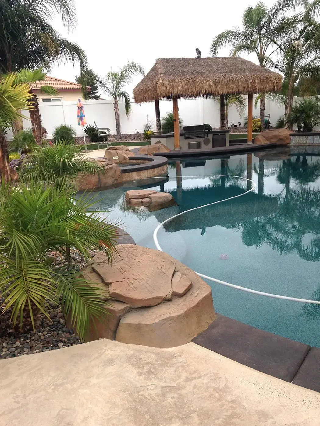 Backyard pool with restained boulders and a thatched palapa