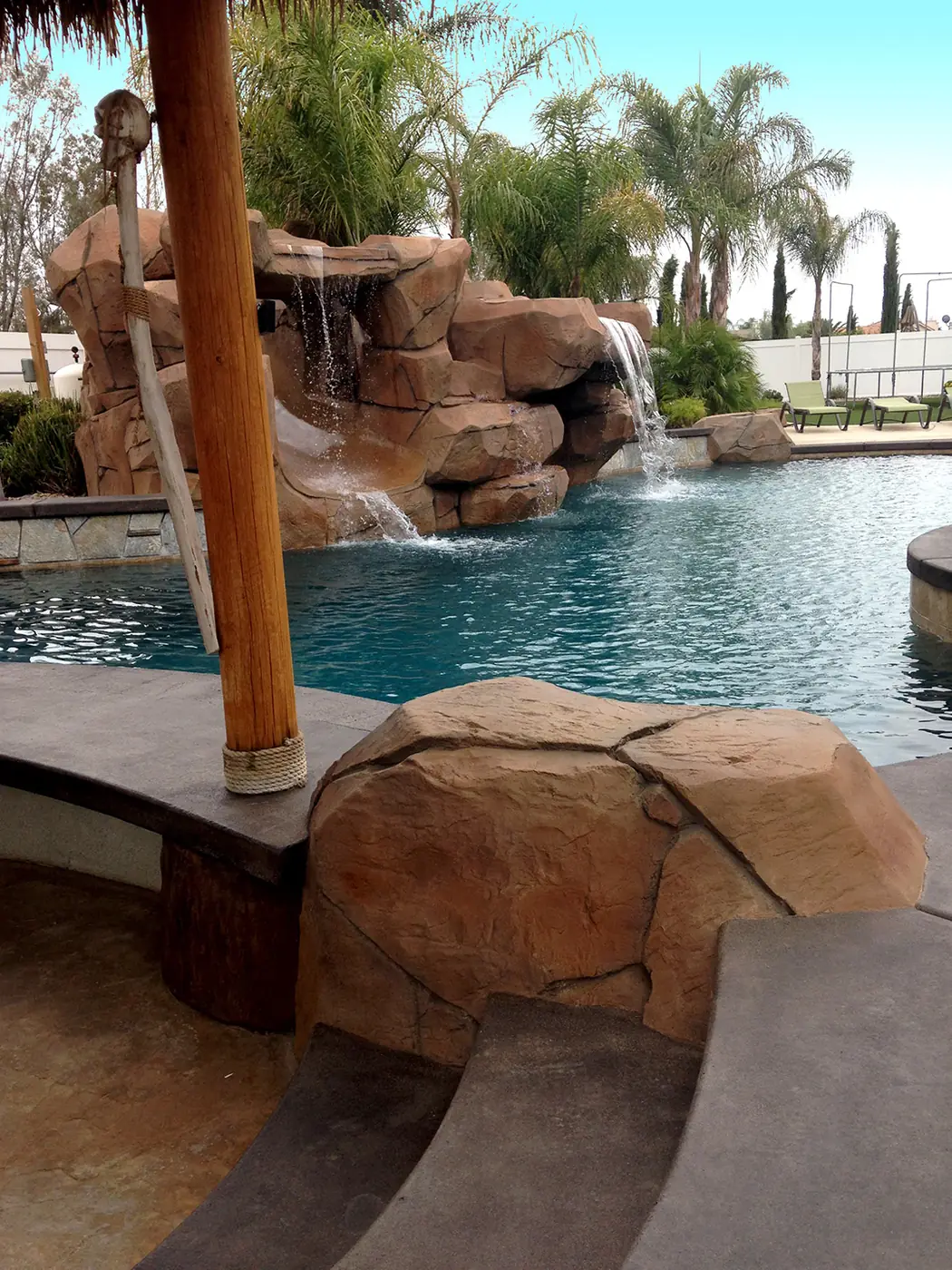 Rock waterfall beside a palapa post at the edge of a pool