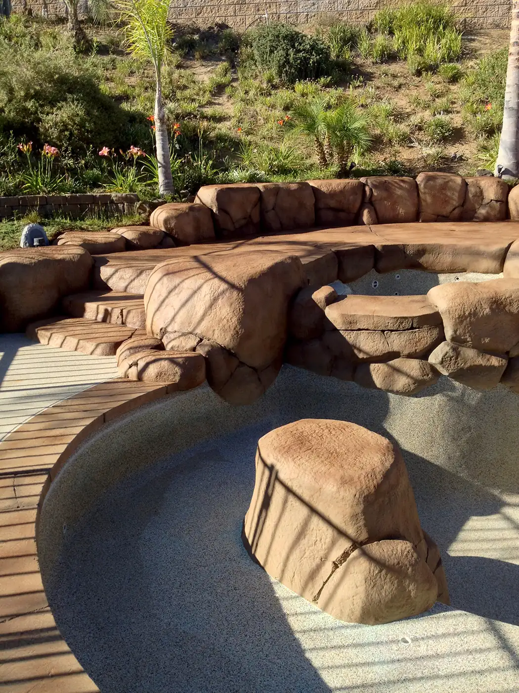 Curved stained deck meeting restained rock at a pool edge
